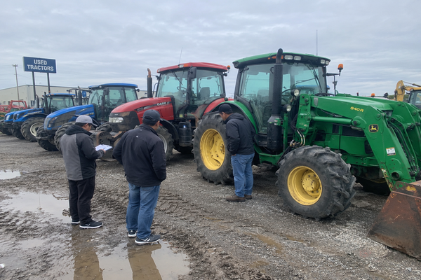 Chinese agricultural equipment buyer comparing several used tractors in a large North American equipment dealership yard while evaluating price, condition, operating hours, and long-term value