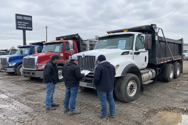 *Buying a used dump truck can be worth it when the savings at purchase are greater than the additional repair risks, maintenance expenses, and operating costs associated with older equipment Commercial truck buyer comparing several used dump trucks in a North American truck yard while evaluating purchase price, dump body condition, hydraulic systems, maintenance history, and long-term business value
